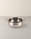 Deep hammered titanium stock pot with two loop handles standing empty on a pale concrete floor against a cream wall