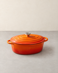 Oval orange enamelled cast iron Dutch oven with its ringed lid, steel knob and two loop handles