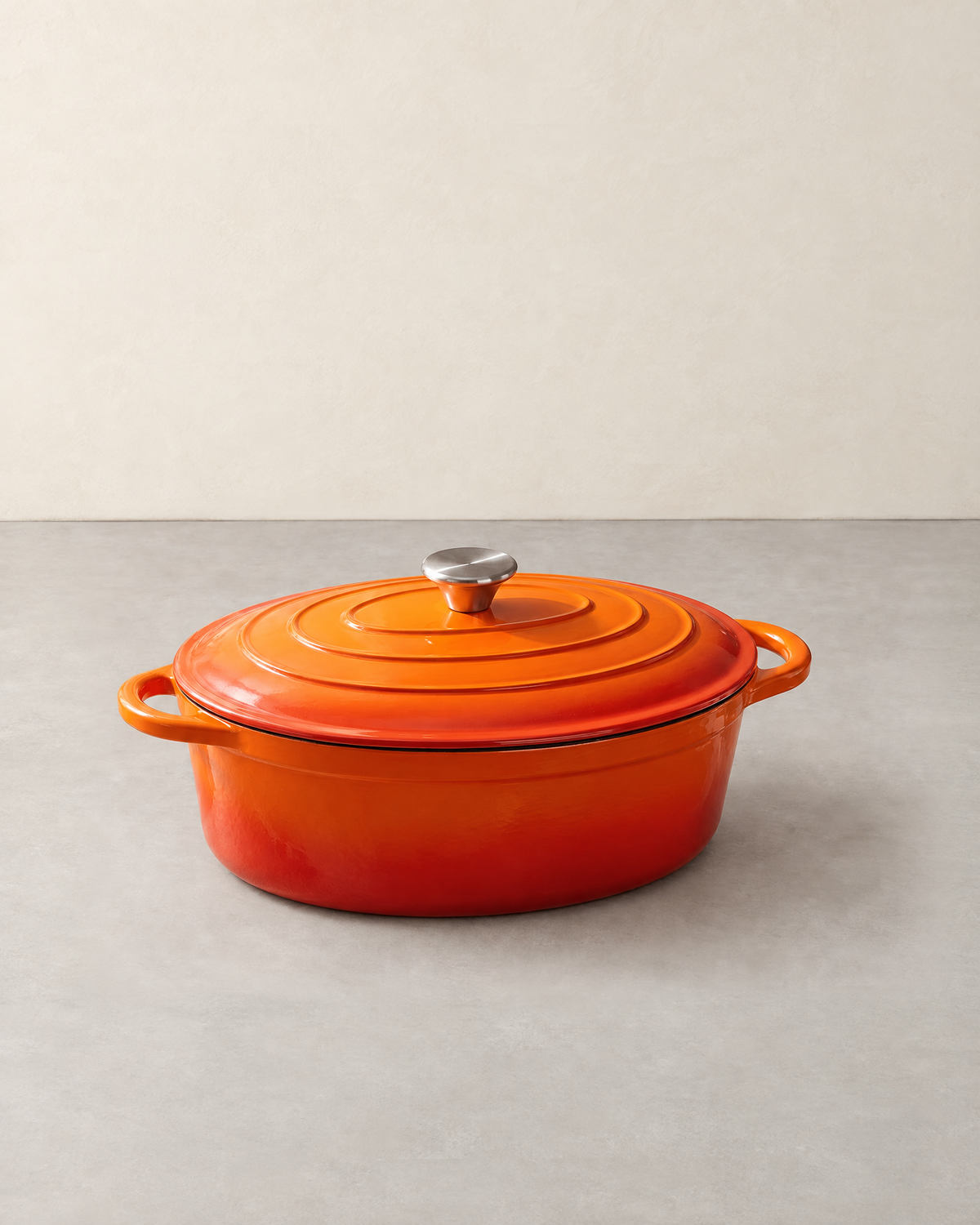 Oval orange enamelled cast iron Dutch oven with its ringed lid, steel knob and two loop handles
