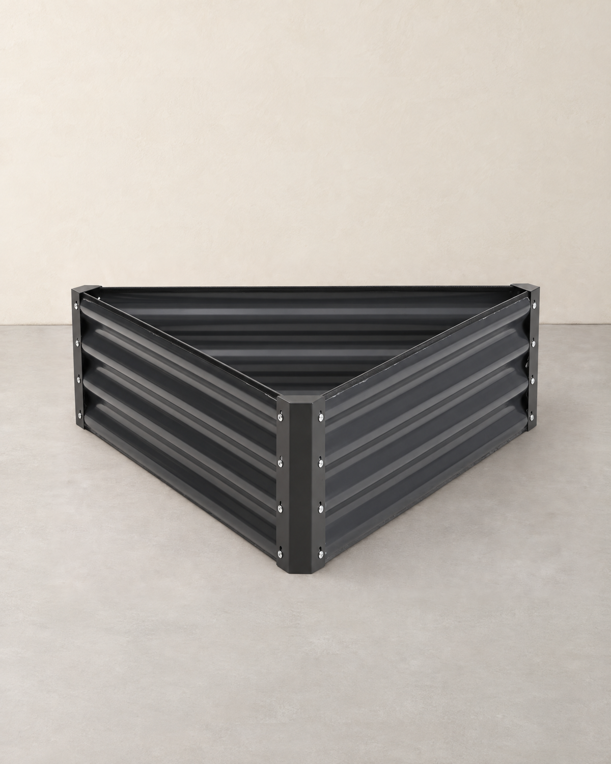 Empty triangular dark grey corrugated steel raised garden bed with bolted corner posts