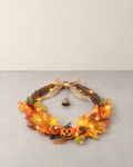 Open woven branch harvest wreath with maple leaves, carved-face pumpkins, a burlap bow and a bell, lying flat