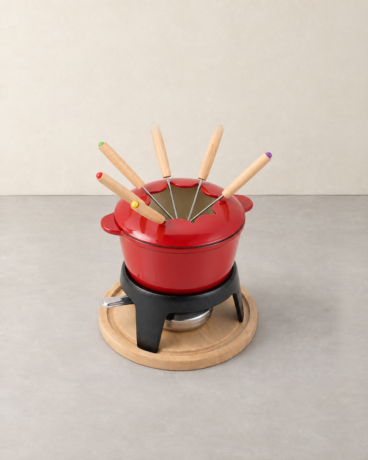 Red enamelled cast iron fondue pot with six colour-tipped forks on a black stand and round wooden base