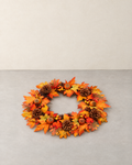 Round orange autumn wreath with maple leaves, pine cones, berry clusters and small pumpkins, lying flat