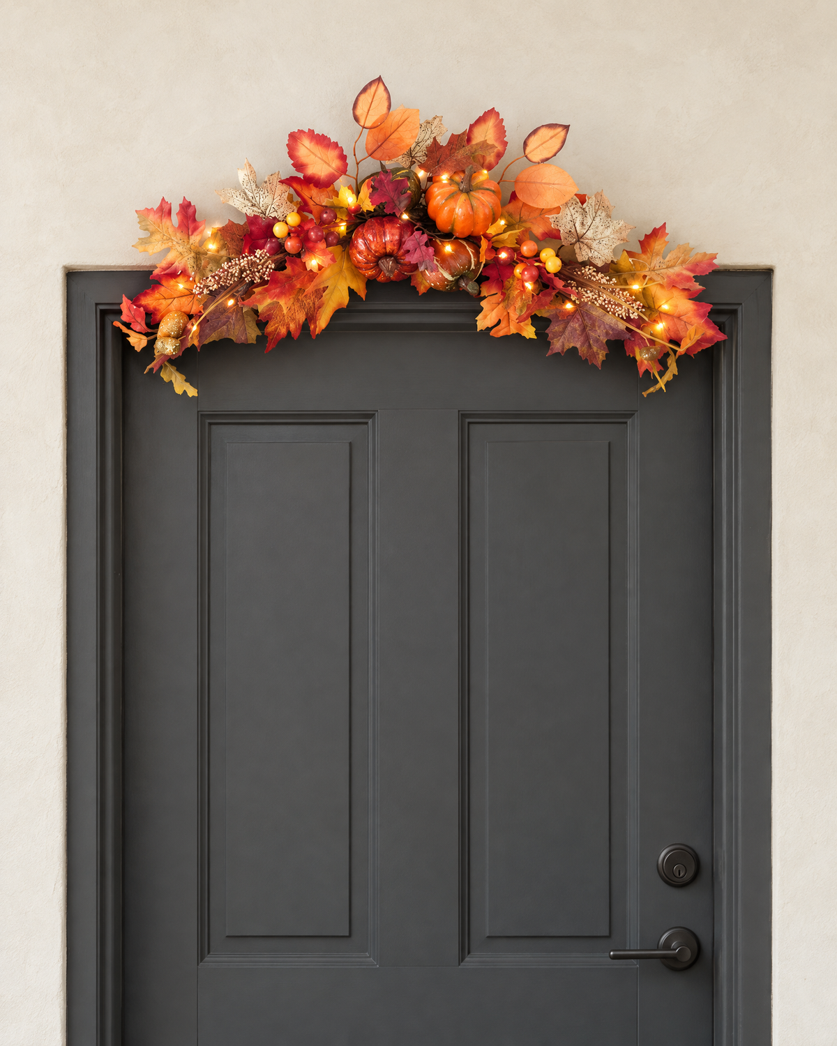 The autumn swag with its lights on, hung across the top of a charcoal front door