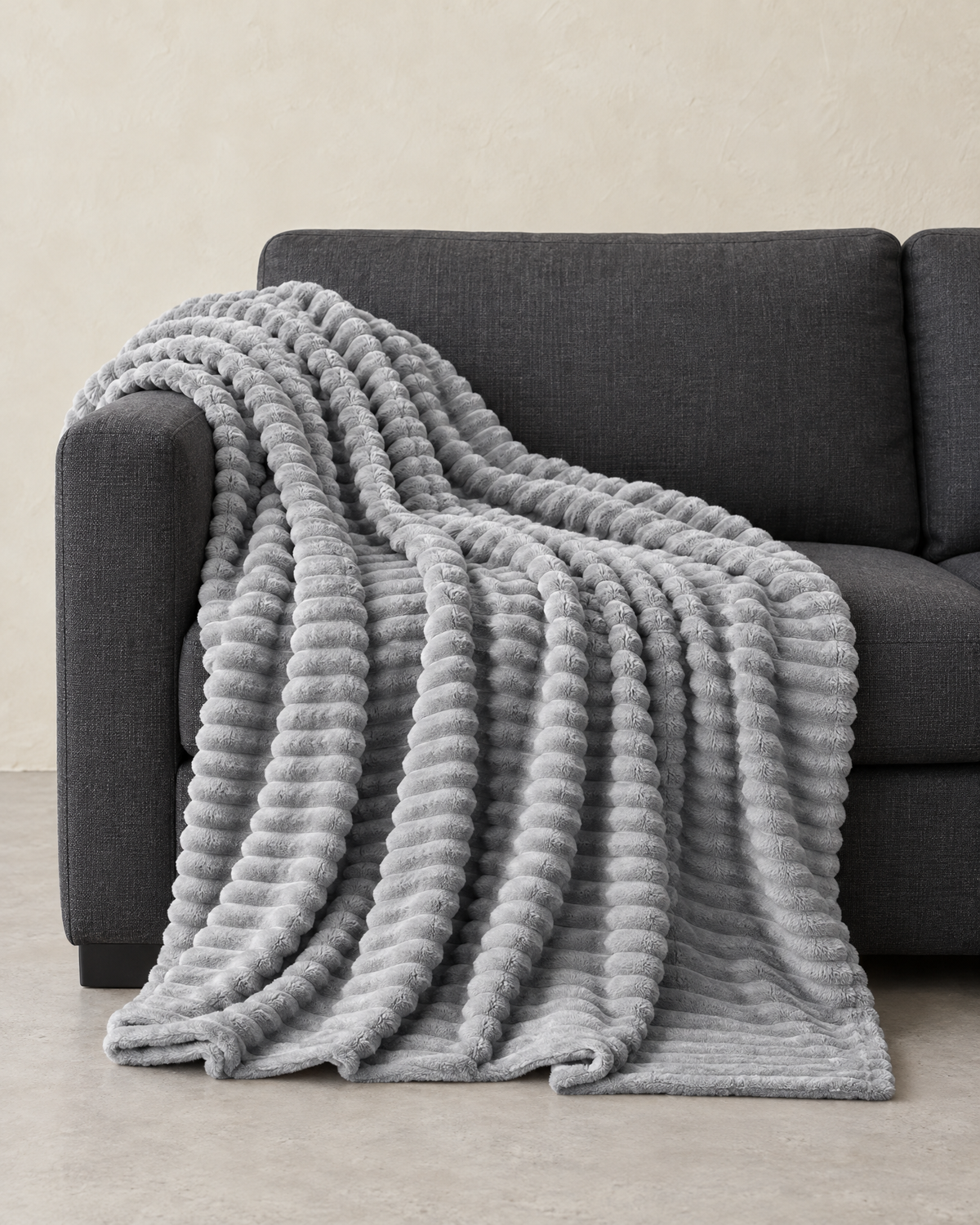 Light grey ribbed plush throw draped over the arm and seat of a charcoal sofa