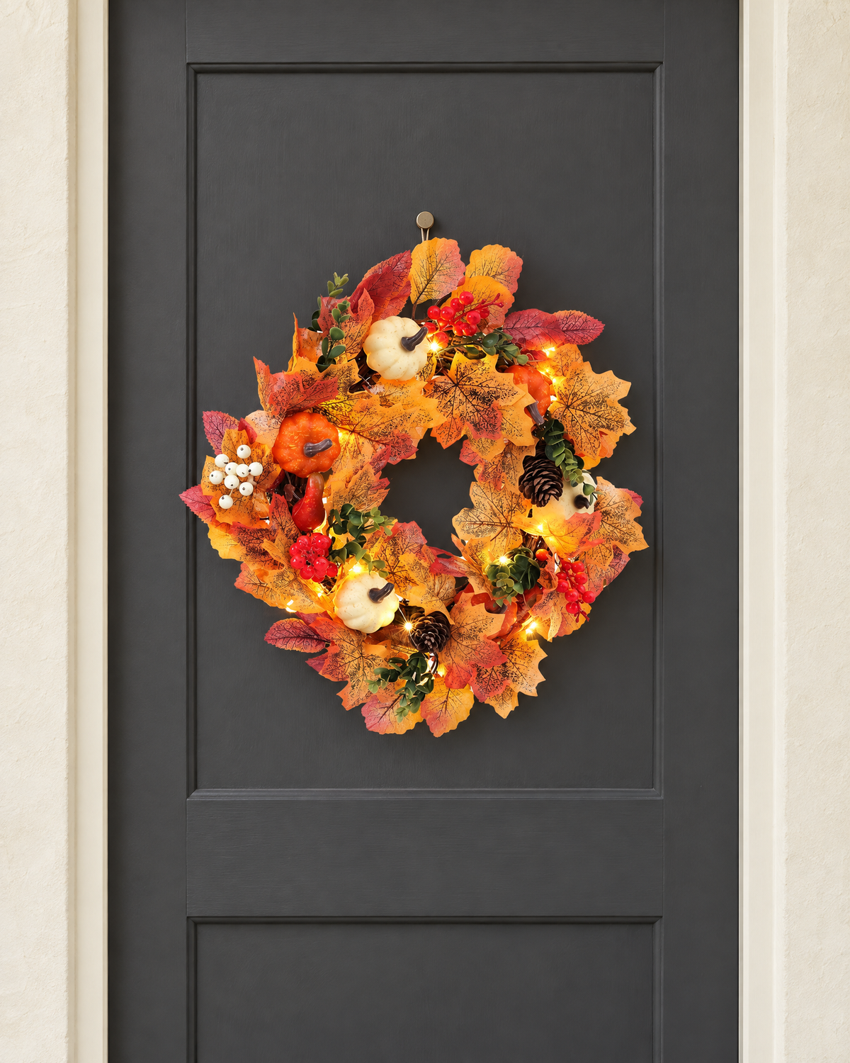 The white and orange pumpkin wreath with its lights on, hung on a charcoal front door