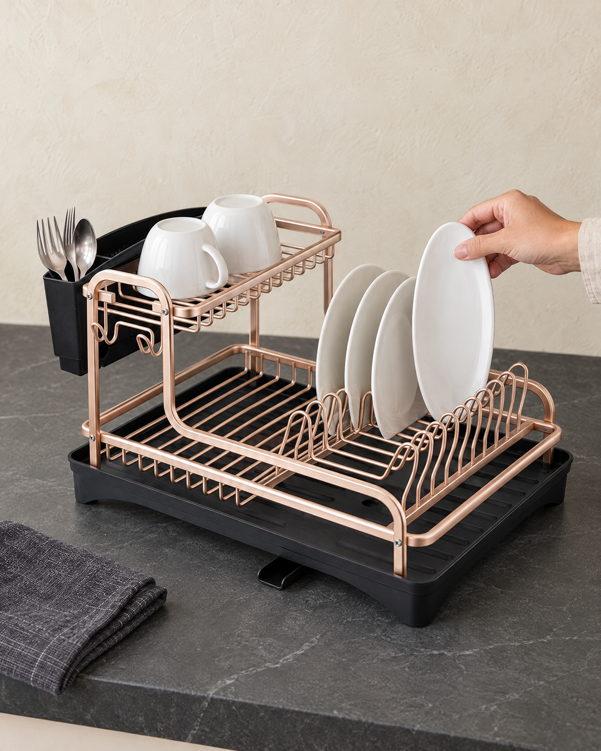 Hand setting a white plate into the rose gold dish rack beside cups and cutlery on a worktop