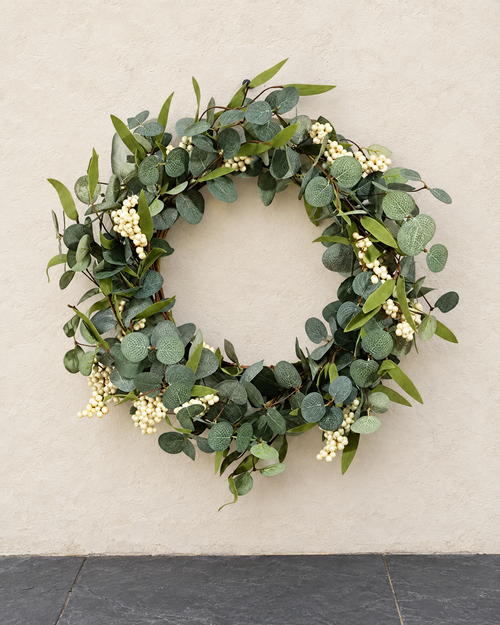 Artificial eucalyptus wreath with white berries hanging on a cream limewashed wall above charcoal slate paving