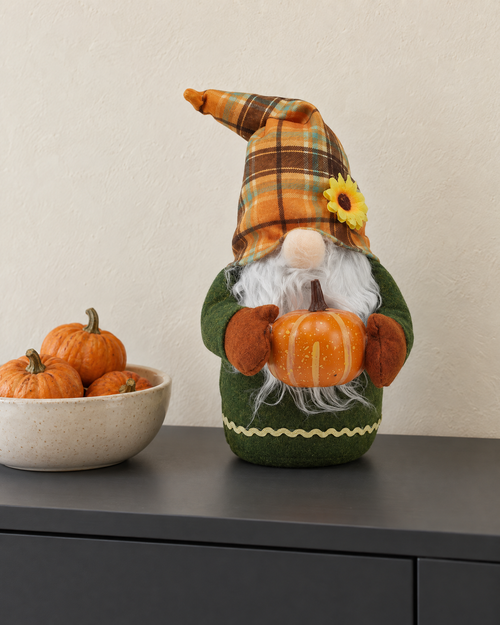 Autumn gnome holding a pumpkin on a charcoal sideboard beside a bowl of small pumpkins