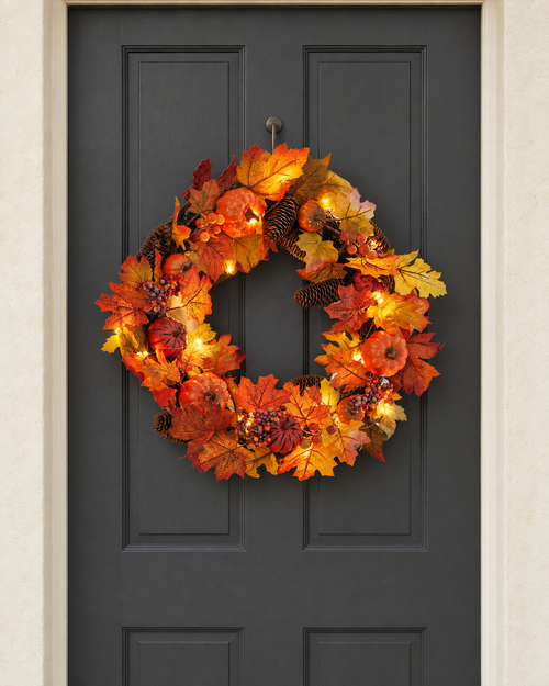 The pumpkin and pine cone wreath with its lights on, hung on a charcoal front door