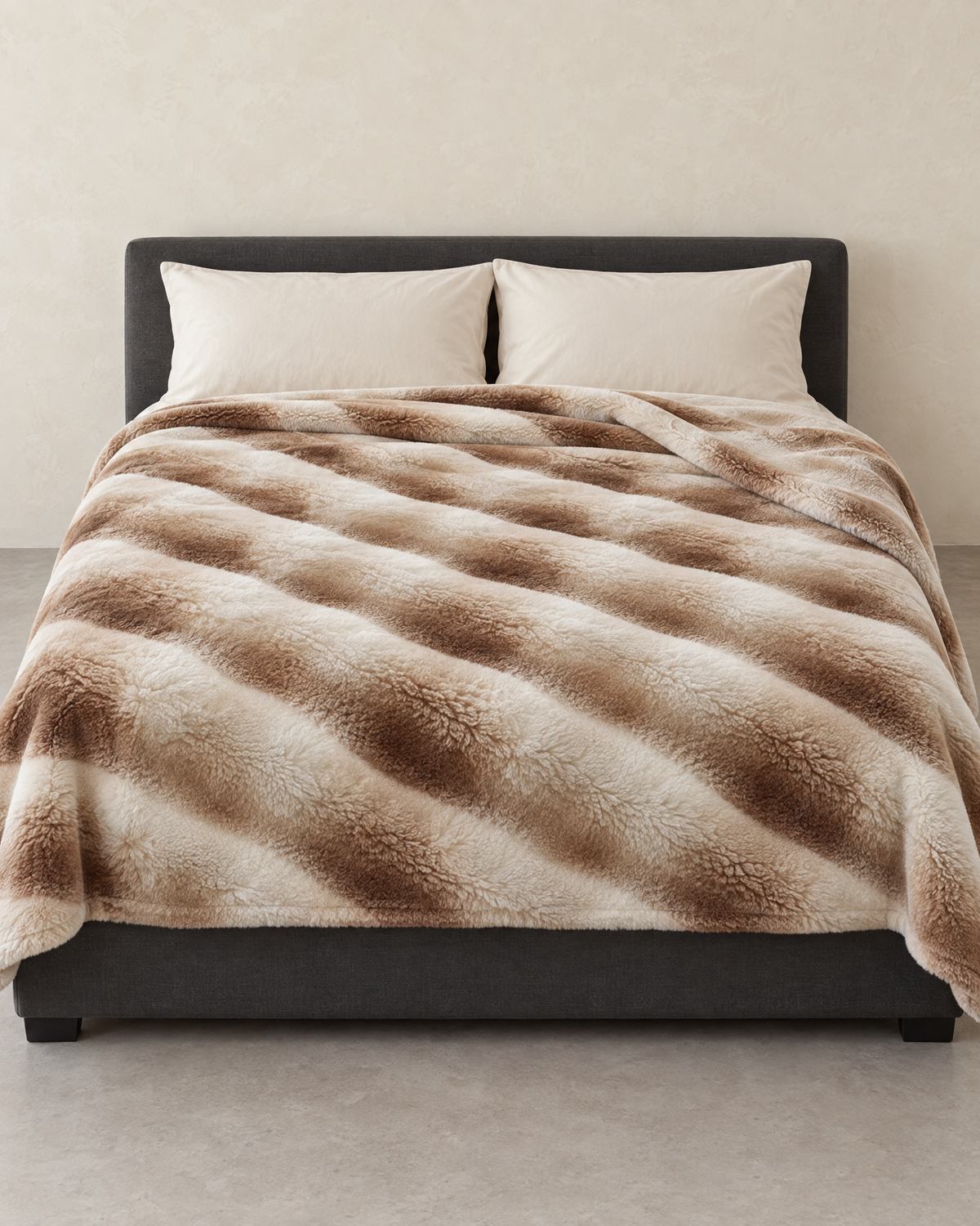 The gradient striped plush blanket spread over a made double bed with cream pillows