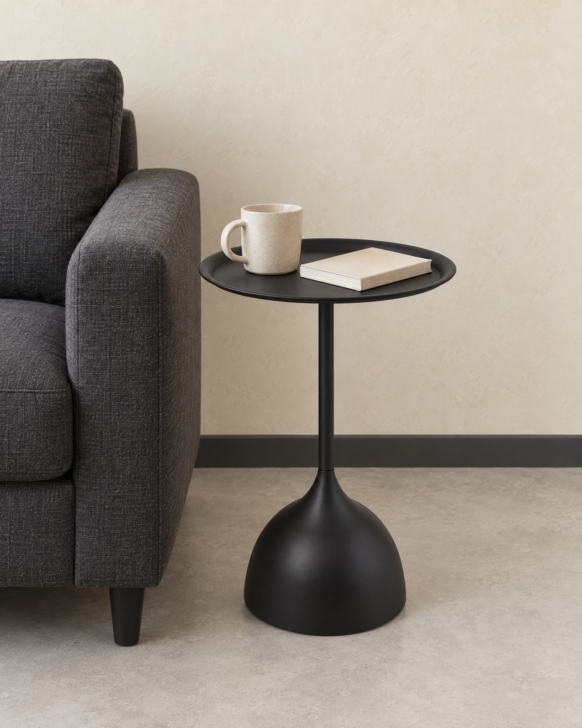 The black round side table beside a grey armchair holding a mug and a book