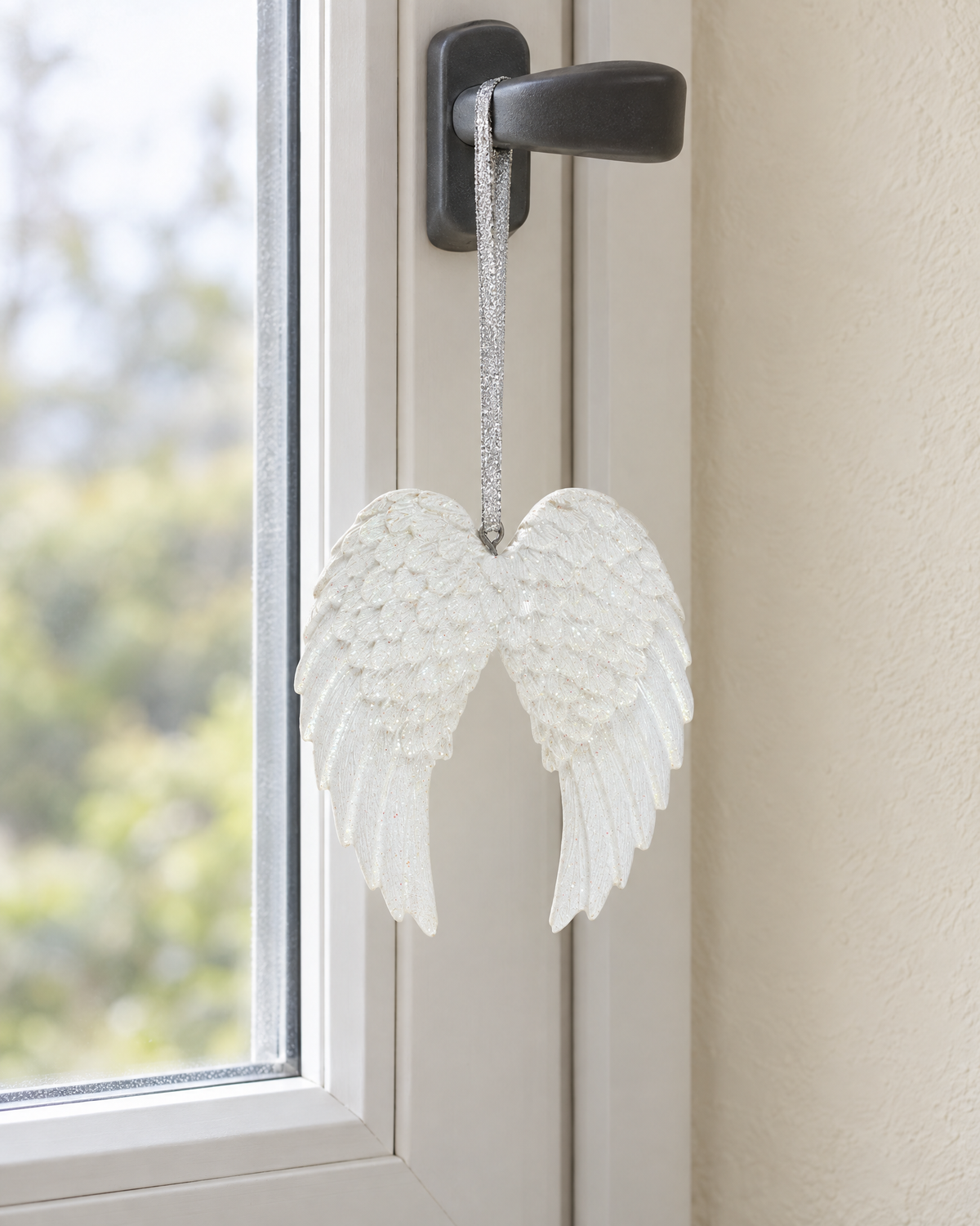 The white glitter angel wings hanging from a window handle in daylight