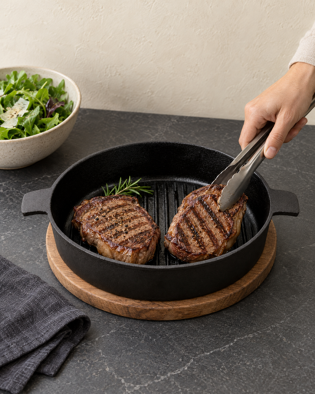 Two rib-eye steaks with grill lines in the ribbed cast iron pan, turned with tongs