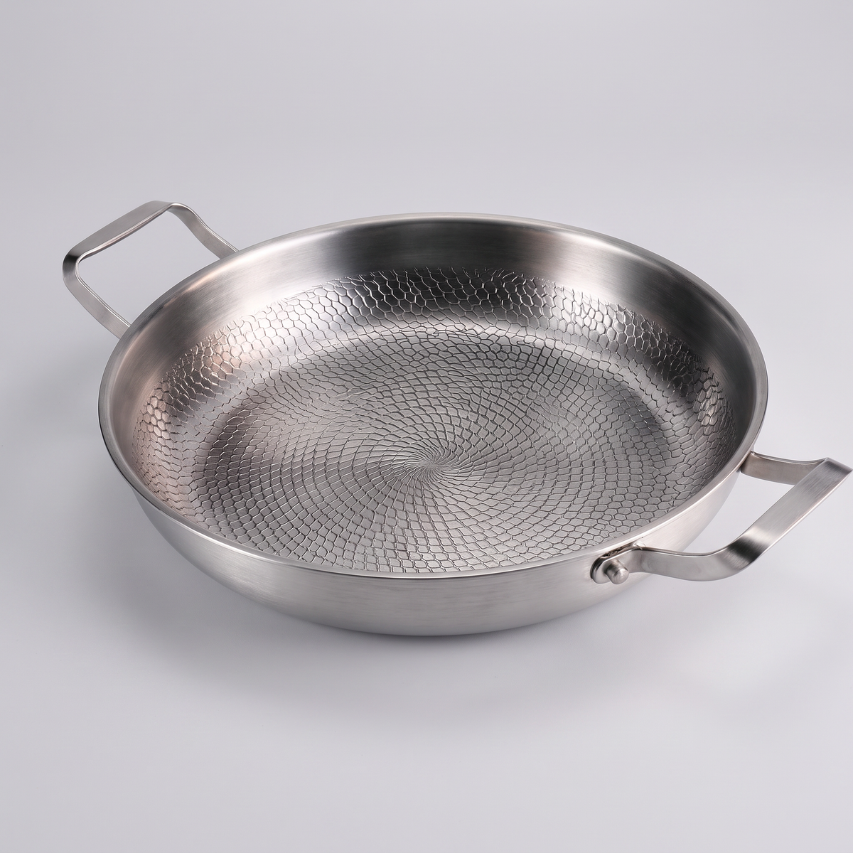Two-handled hammered metal sauté pan on a seamless pale grey paper sweep.