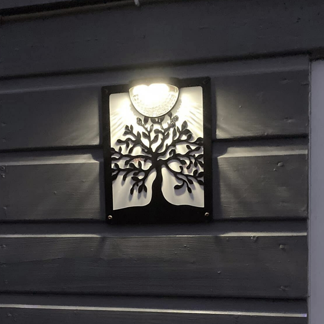 Tree of life solar plaque lit at night on dark wooden cladding