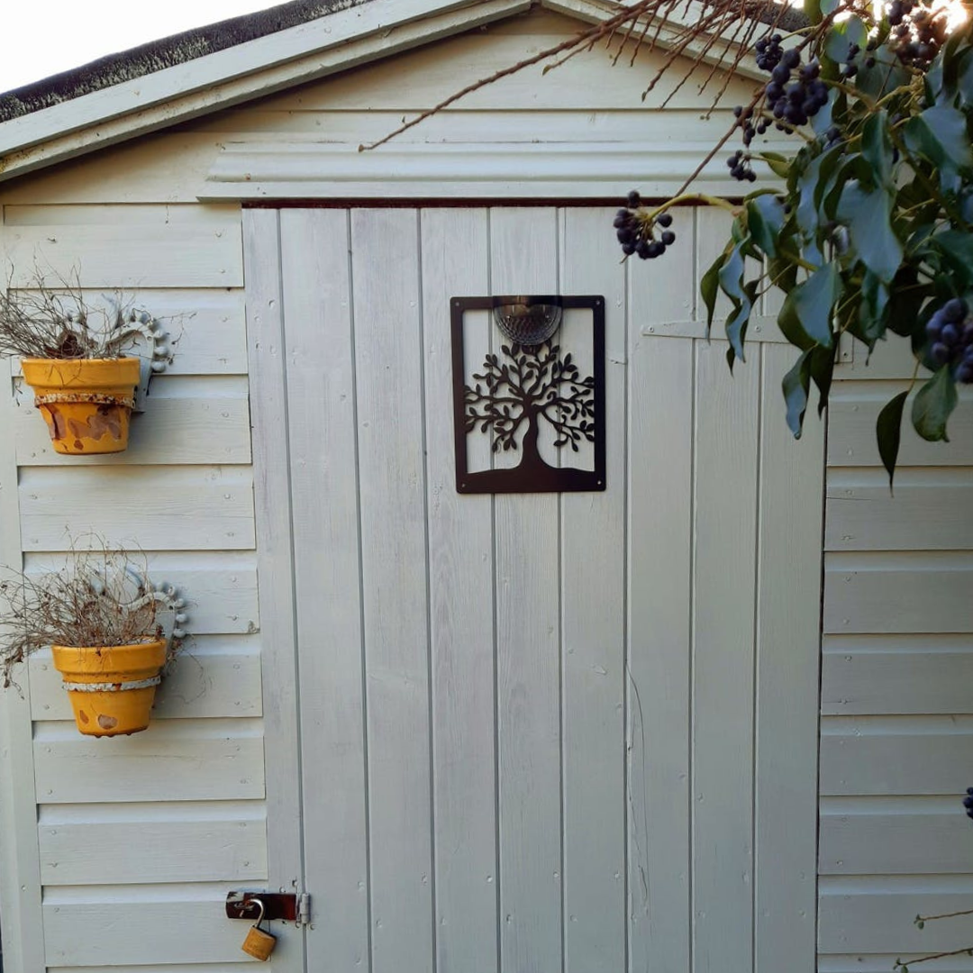 Tree of life solar plaque on a cream shed door between two hanging pots
